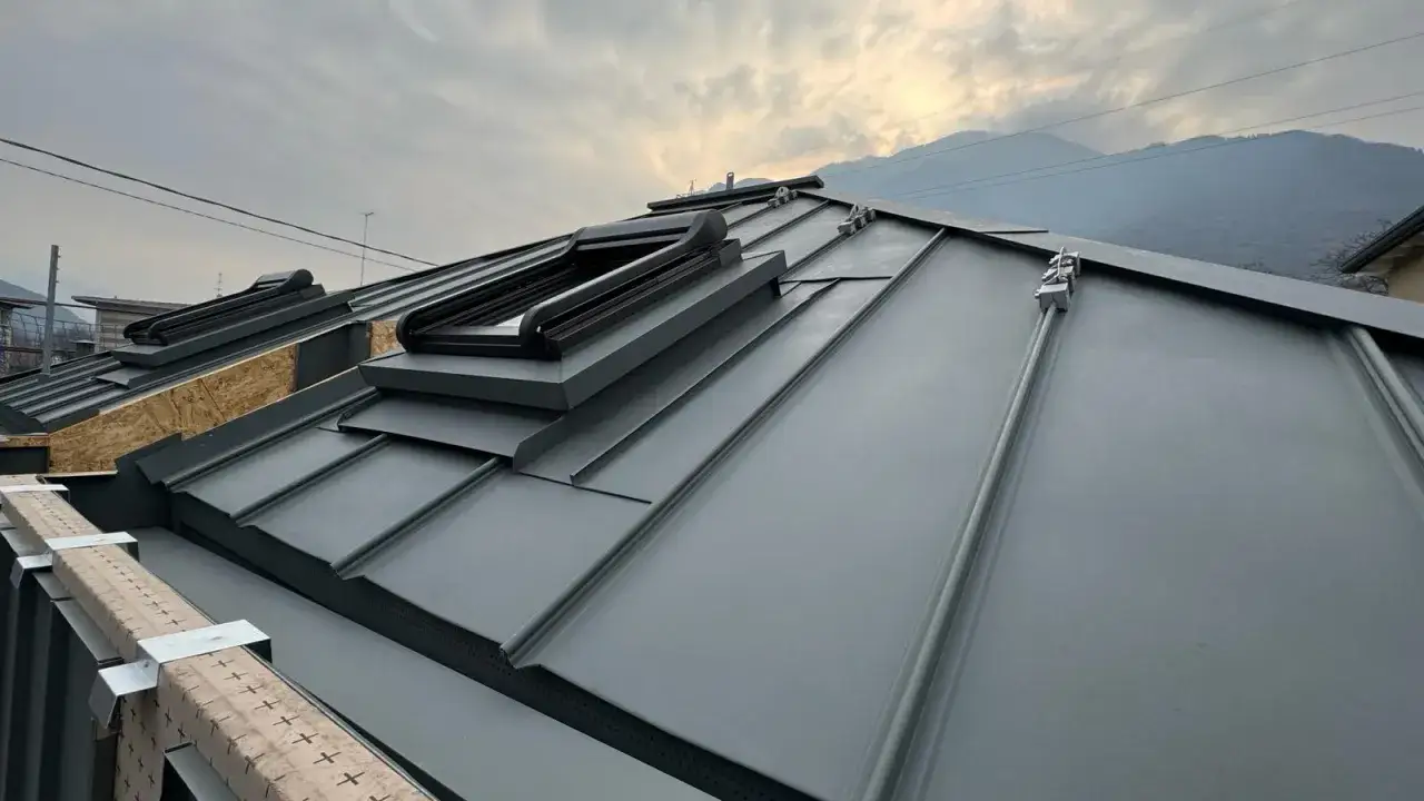 Tegole tetto moderne in metallo grigio, con lucernari integrati, su uno sfondo di montagne nebbiose.