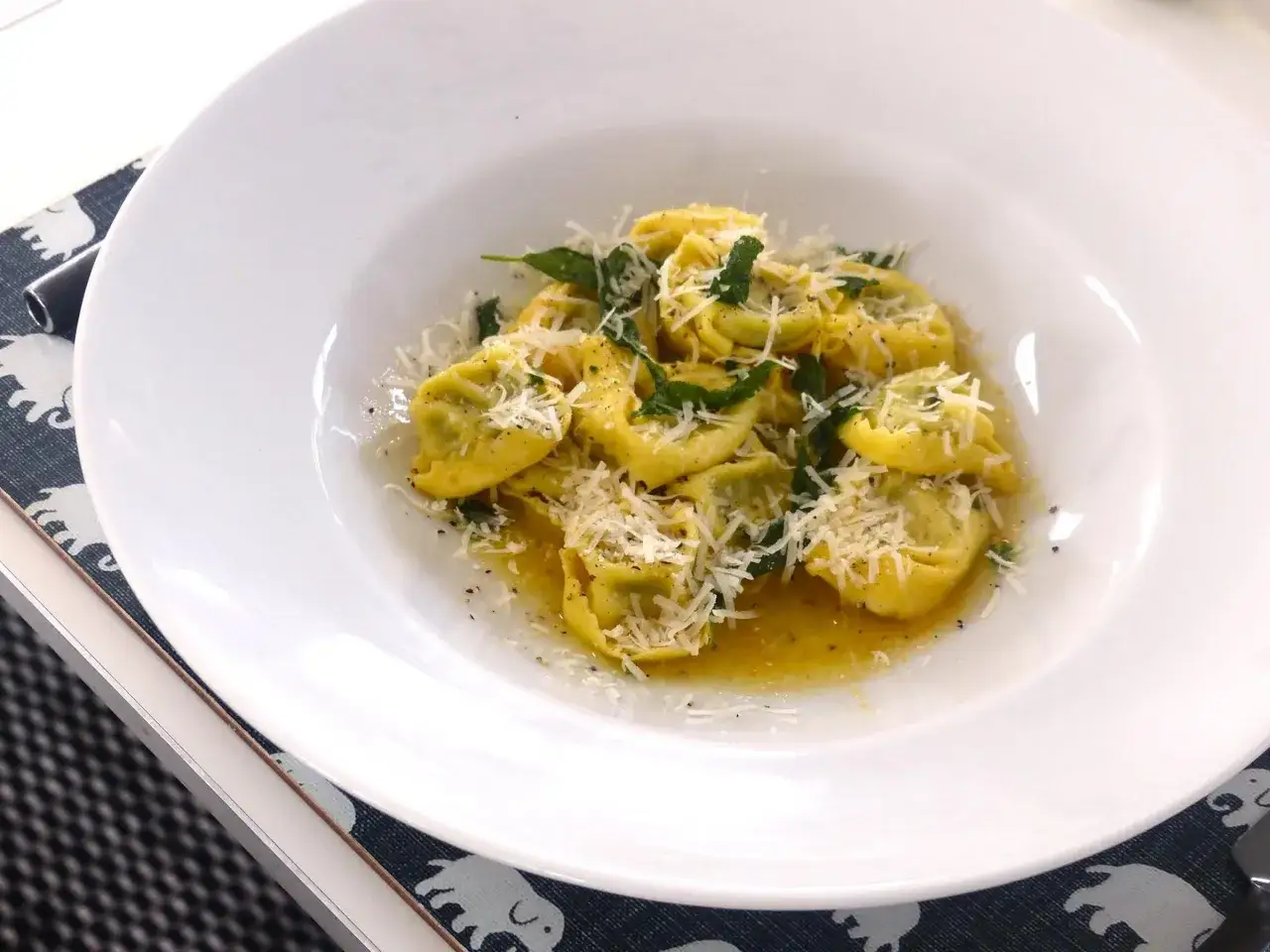 En tallrik med tortellini prosciutto, toppad med riven parmesan och f&auml;rska &ouml;rter.