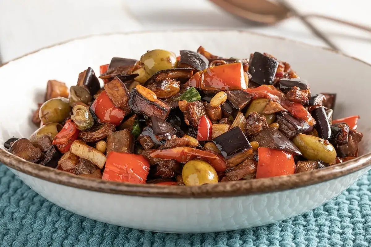 Caponata ricetta semplice: melanzane, peperoni, olive e capperi in un piatto invitante.