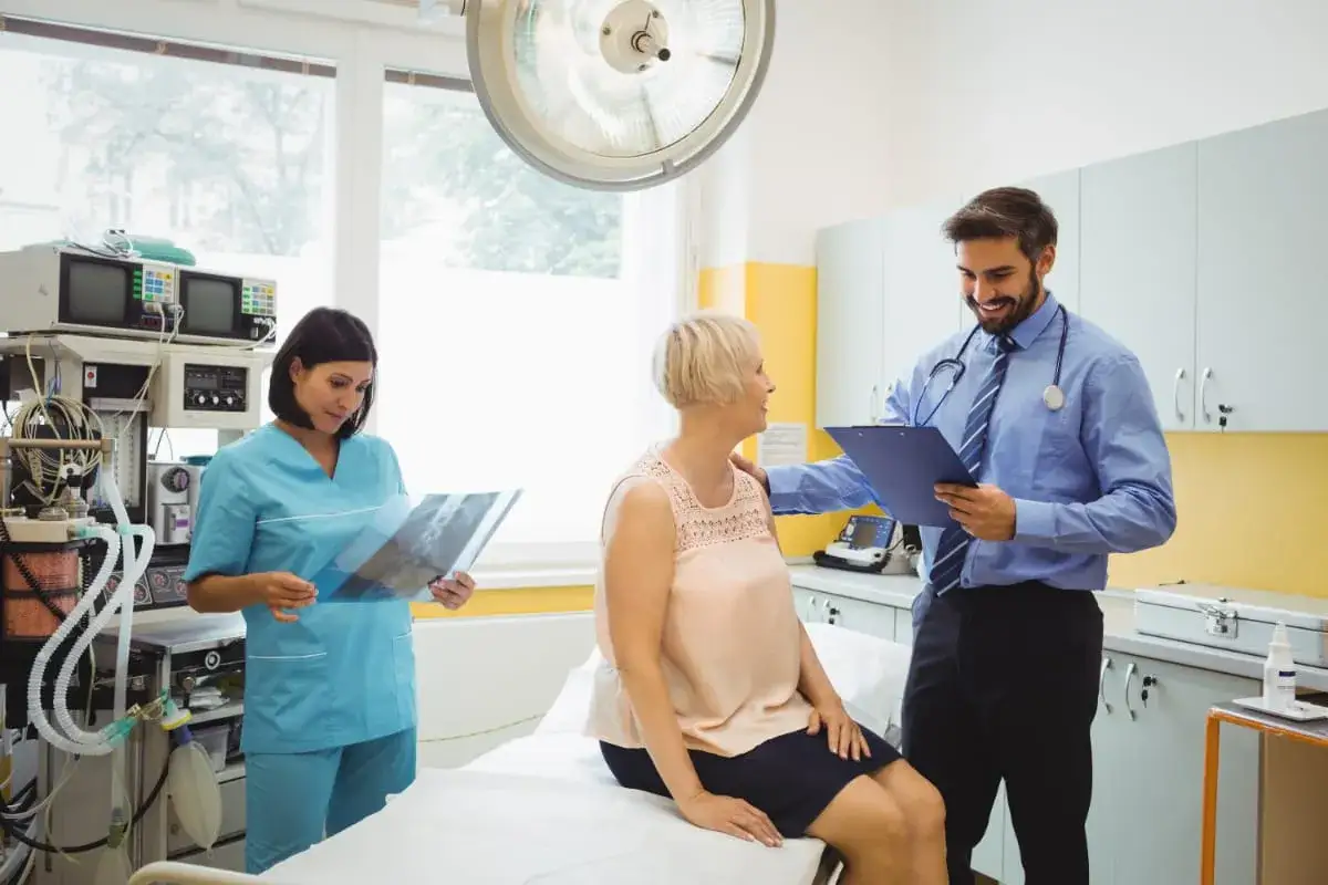 Lekarz omawia z pacjentką wyniki badań, pielęgniarka analizuje rentgen. Widoczny objaw kliniczny.