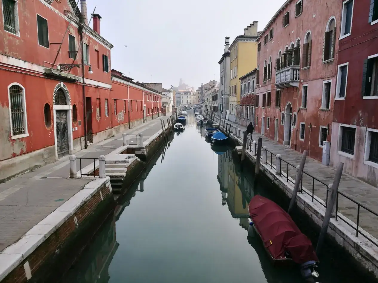 Un uomo osserva le vie di Venezia, un canale tranquillo fiancheggiato da case colorate e barche ormeggiate.