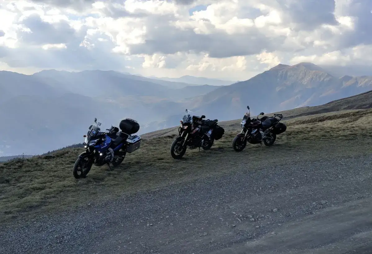 Tre moto parcheggiate sul crinale del passo dell'Abetone, con un panorama montuoso mozzafiato sotto un cielo nuvoloso.