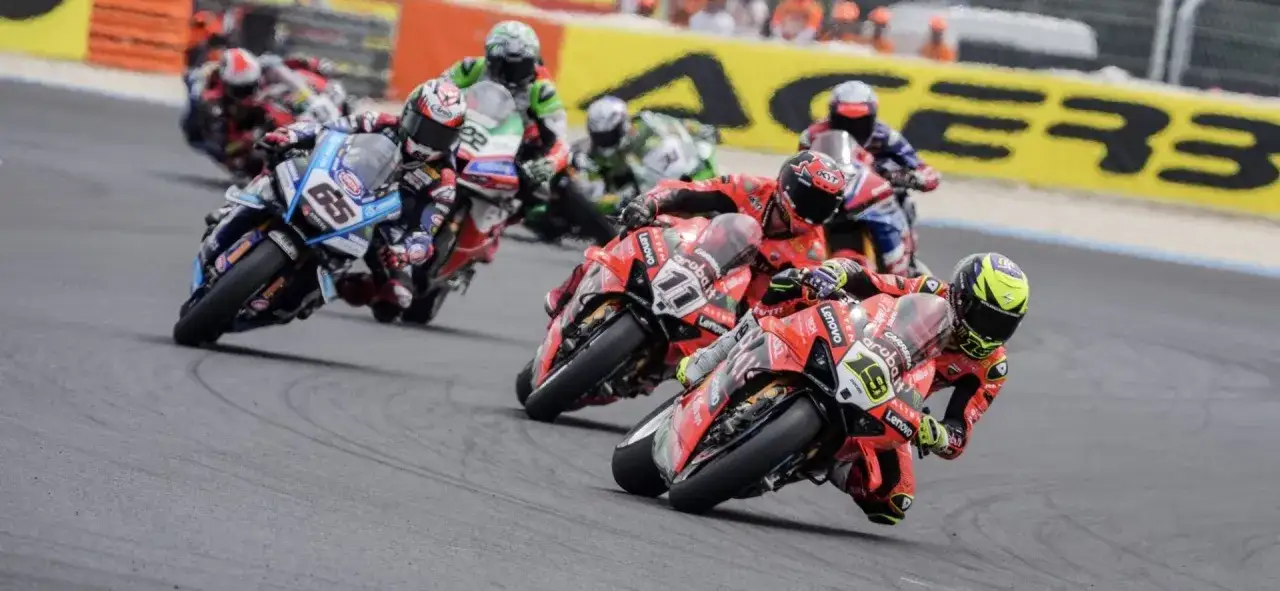 Motociclistas compiten en una carrera, con el número 65 en primer plano. ¡Consulta el horario SBK hoy para no perderte la acción!