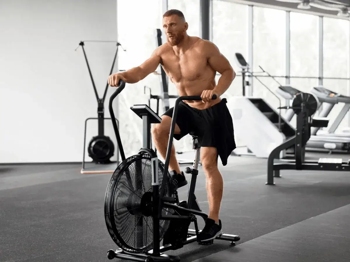 Mężczyzna w pełni sił wykonuje intensywny trening cardio na rowerze stacjonarnym w siłowni.