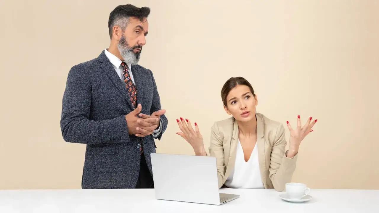 Un collega che vuole comandare, con un'espressione autoritaria, parla a una collega che sembra confusa e frustrata.