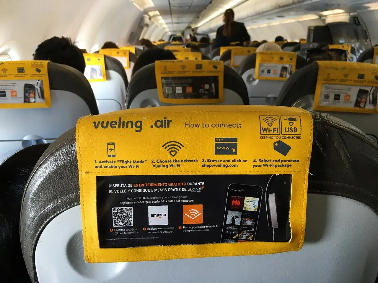 Wnętrze samolotu Vueling, żółte zagłówki z instrukcją połączenia z Wi-Fi i informacją o bagażu podręcznym.