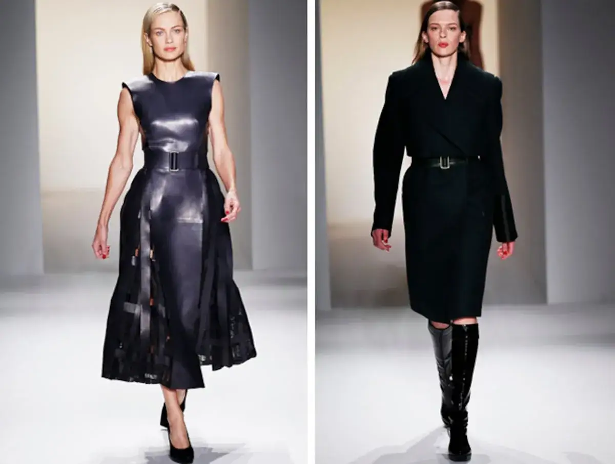 Modelos desfilan creaciones de Calvin Klein (diseñador): un vestido de cuero negro con falda plisada y un conjunto de abrigo y falda oscuros con botas altas.