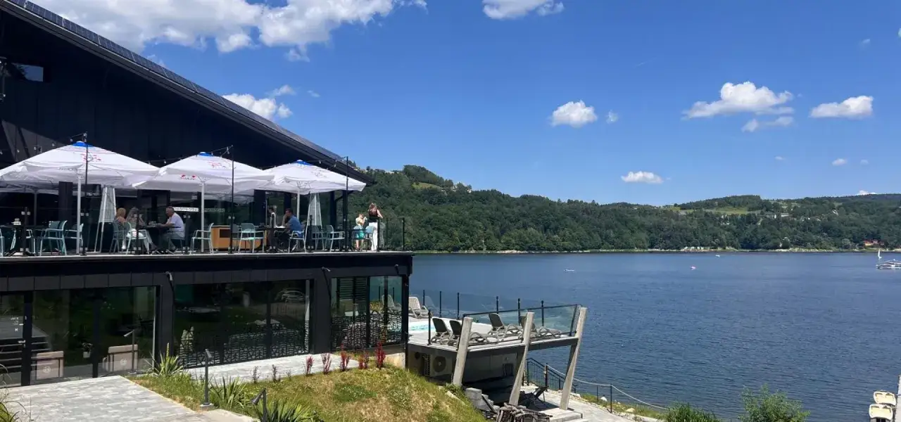 Relaks nad Jeziorem Rożnowskim. Taras restauracji z widokiem na wodę, zielone wzgórza i błękitne niebo. Idealne miejsce na podziwianie atrakcji.