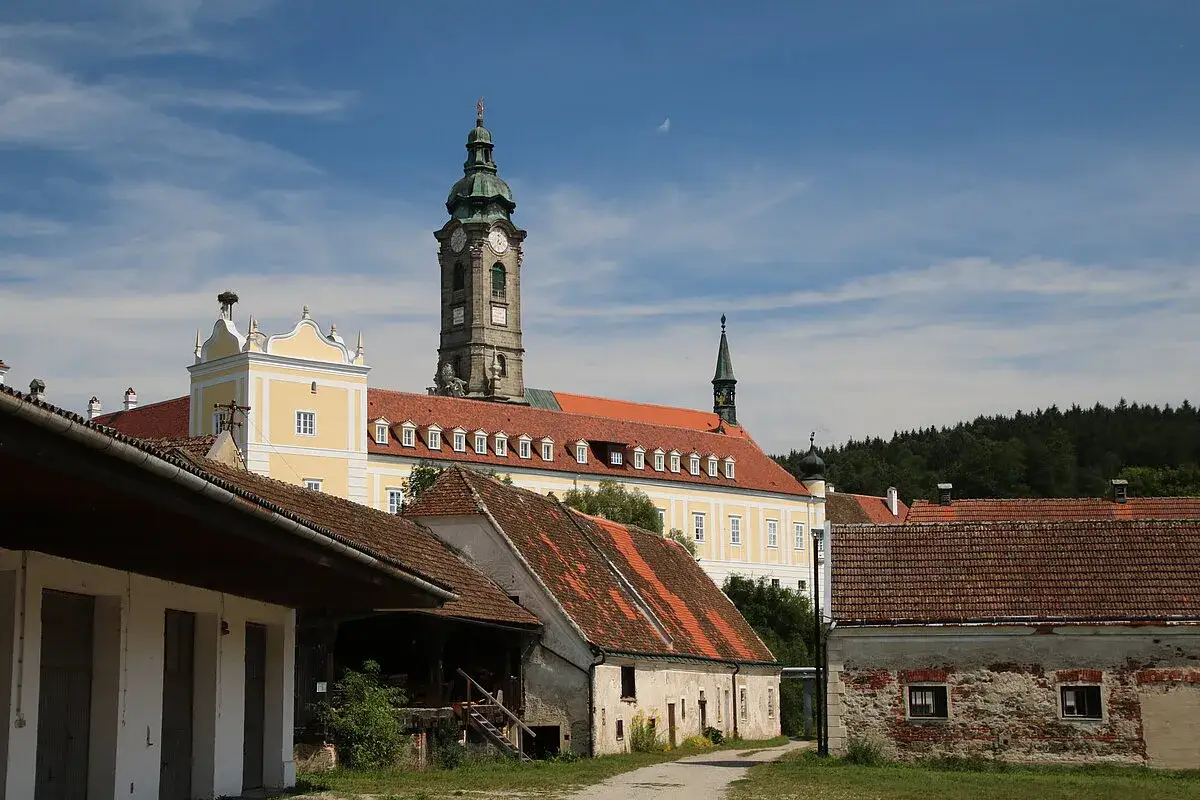 Das Stift Zwettl, ein imposantes Kloster mit markantem Turm, ragt hinter alten Wirtschaftsgebäuden auf.