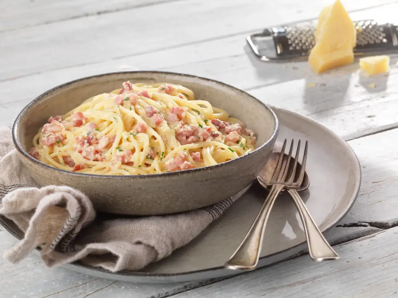 Un plat de tagliatelles carbonara cr&eacute;meuses, garni de lardons et de persil, servi dans un bol en c&eacute;ramique sur une assiette grise.