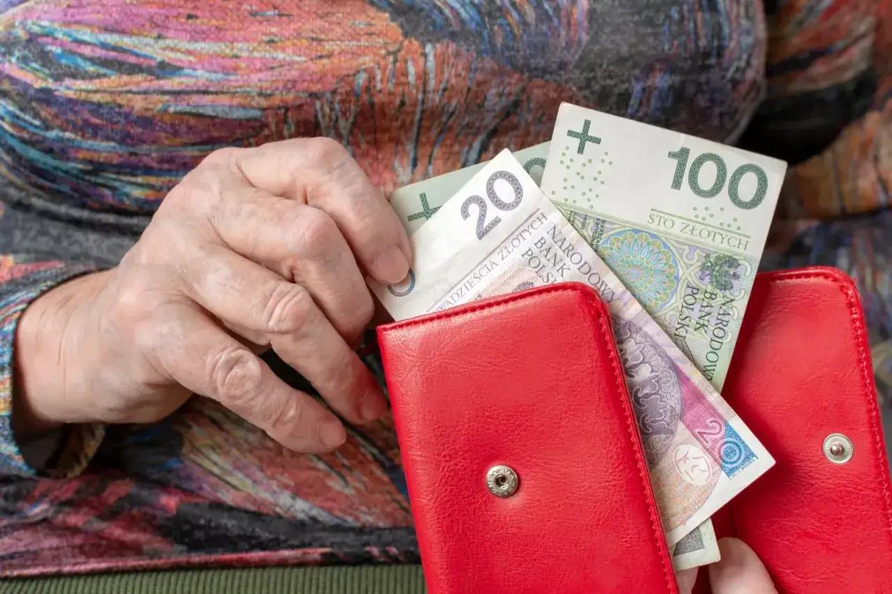 Dłoń starszej osoby wkłada polskie złotówki do czerwonego portfela. Zastanawiasz się, w jakim miesiącu najlepiej przejść na emeryturę?