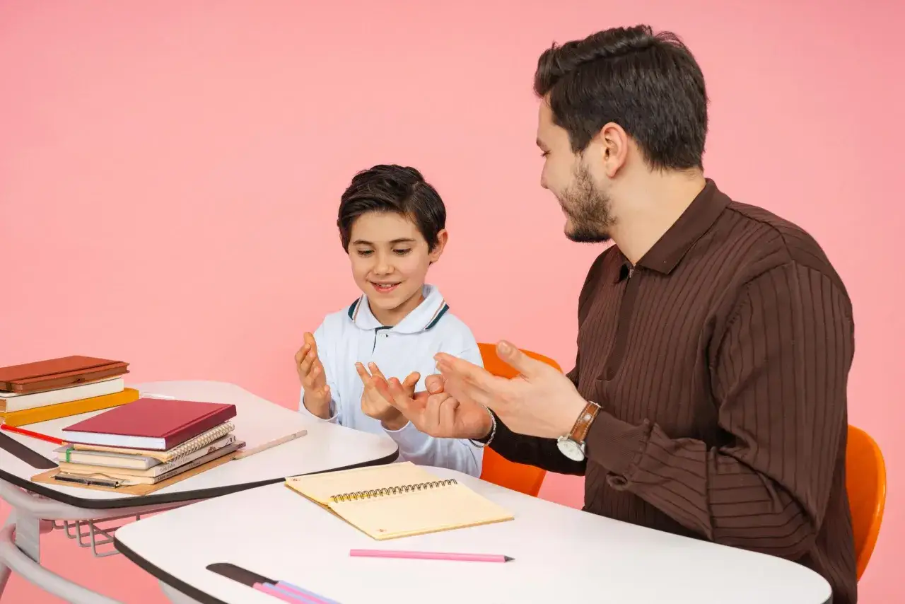 Un uomo e un bambino interagiscono con le mani, mostrando una **relazione educativa** positiva. Libri e quaderni sono disposti sulla scrivania.