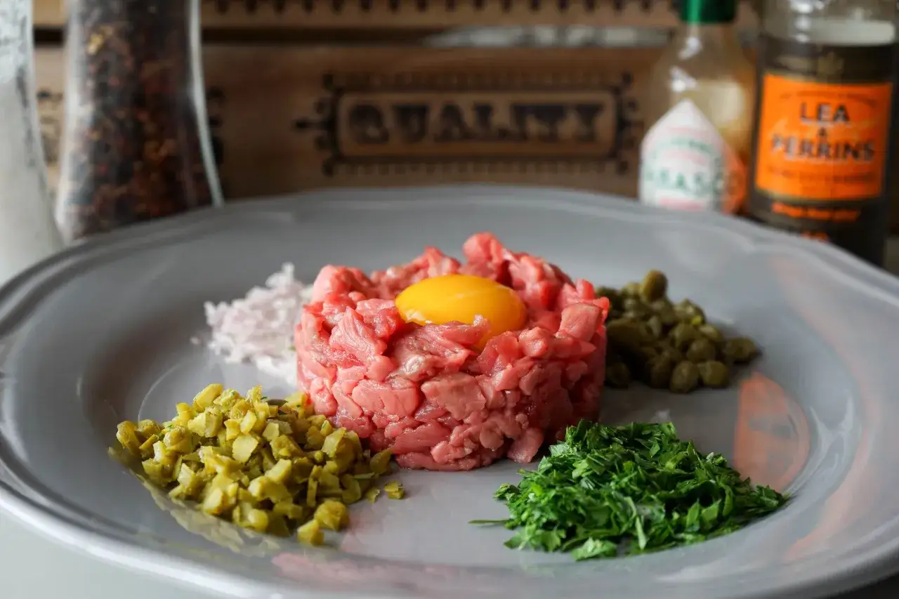 Un plat de tartare de bœuf frais, garni d'un jaune d'œuf, avec des câpres, des cornichons hachés, des échalotes et du persil.