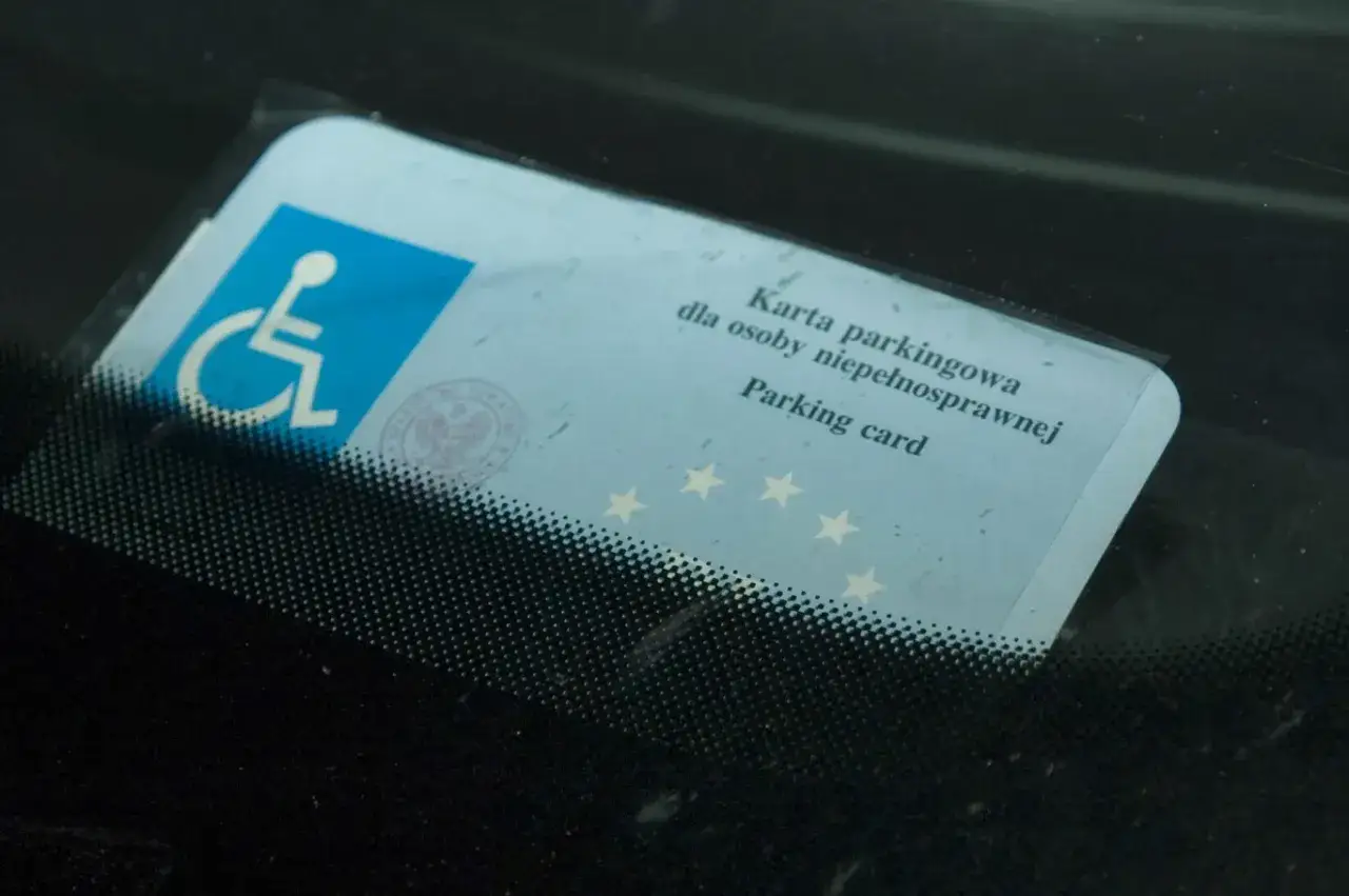 Karta parkingowa z symbolem niepełnosprawności, umieszczona za przednią szybą samochodu.