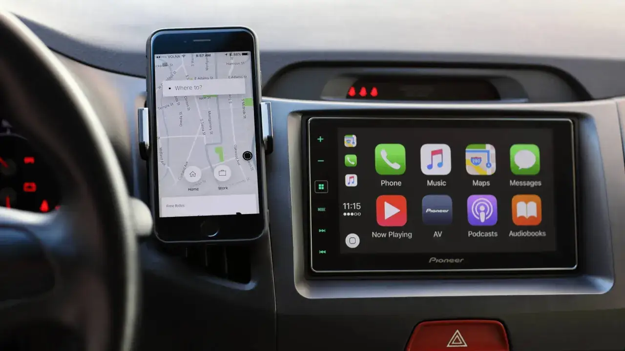 Jak połączyć telefon z samochodem? Smartfon z nawigacją Uber zamontowany na desce rozdzielczej, obok ekranu systemu Pioneer z ikonami aplikacji.