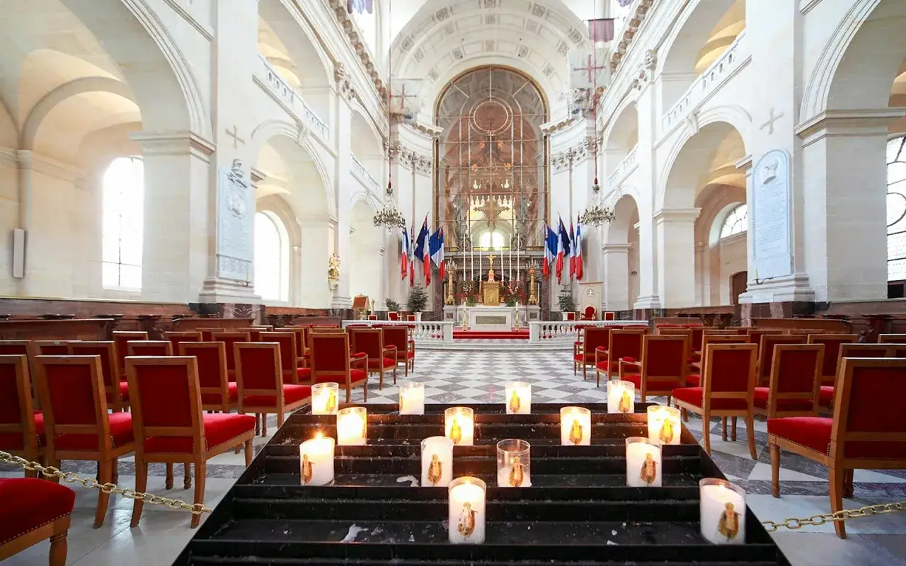 Interior de la Catedral de San Luis de los Inv&aacute;lidos, con filas de sillas rojas y velas encendidas en el altar.