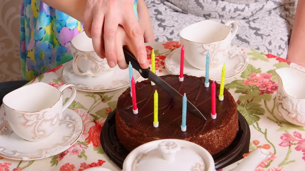 Ręka kroi czekoladowy tort ze świeczkami. Zobacz, jak kroić tort, by każdy dostał kawałek!