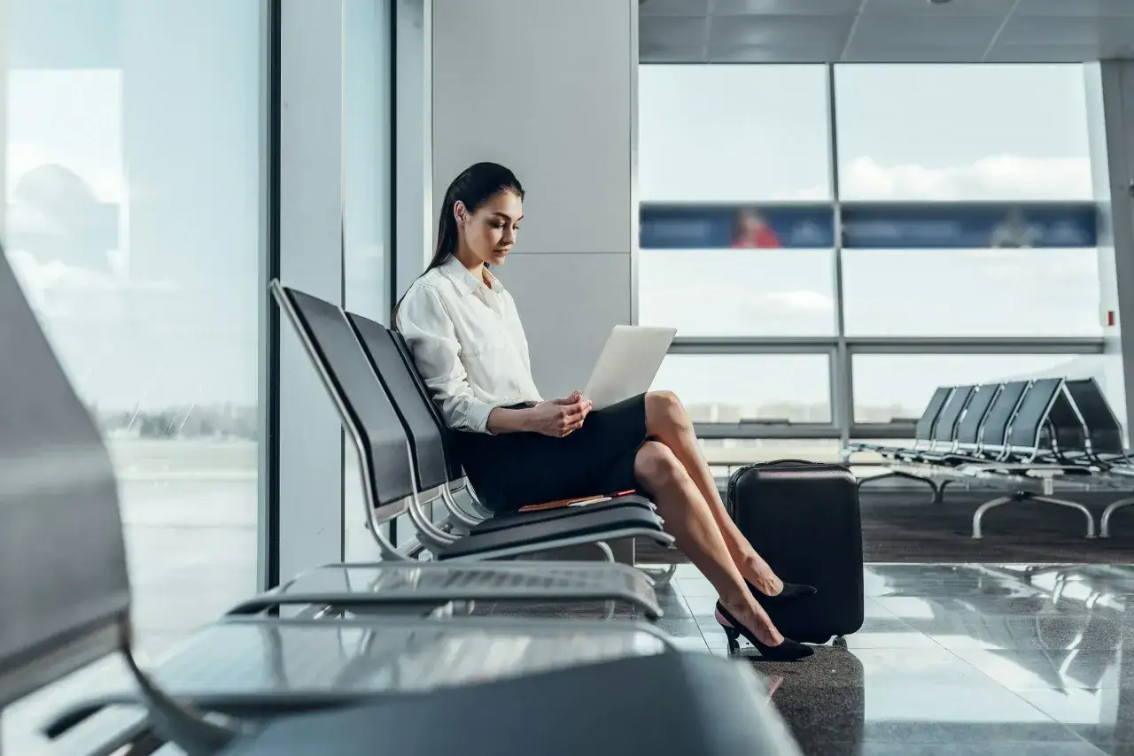 Junge Frau mit Laptop im Flughafen-Wartebereich, bereit f&uuml;r ihr bezahltes Auslandspraktikum.