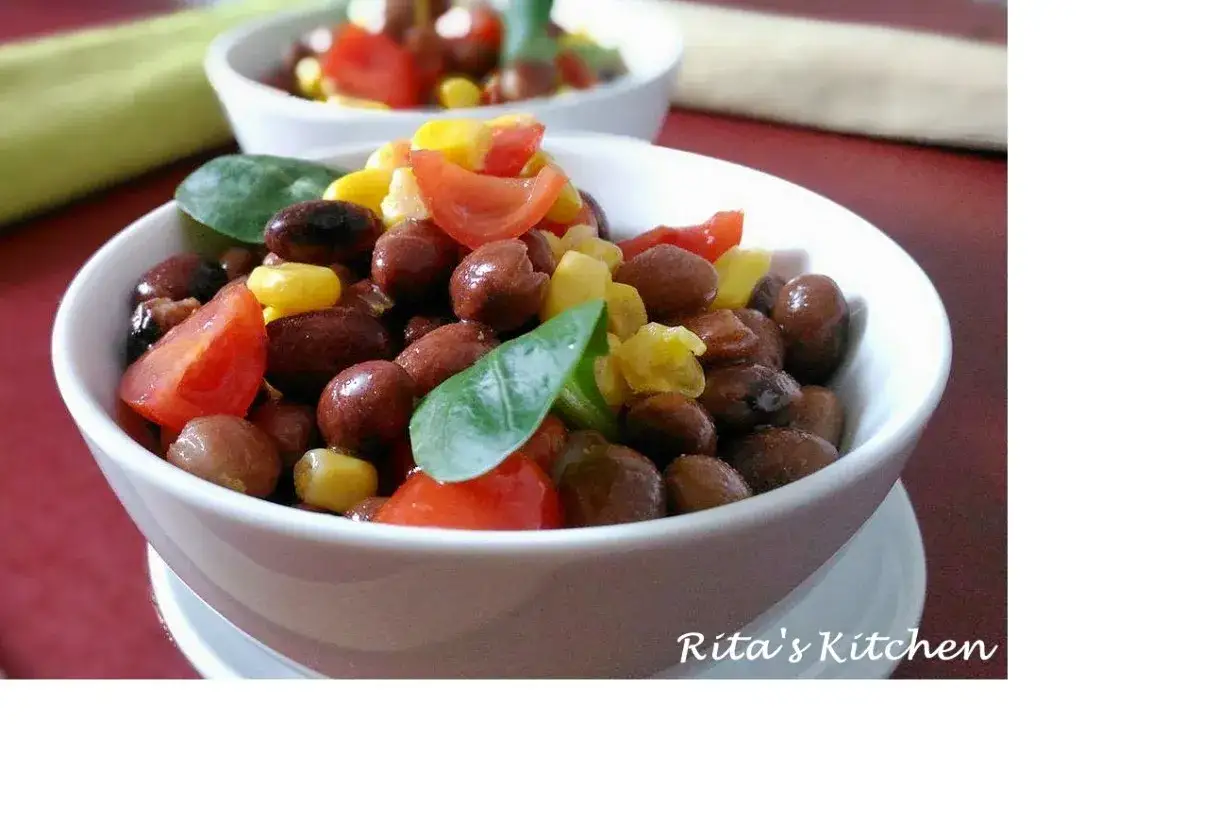 Un'insalata di fagioli sfiziosa con pomodorini, mais e foglie verdi, servita in una ciotola bianca.