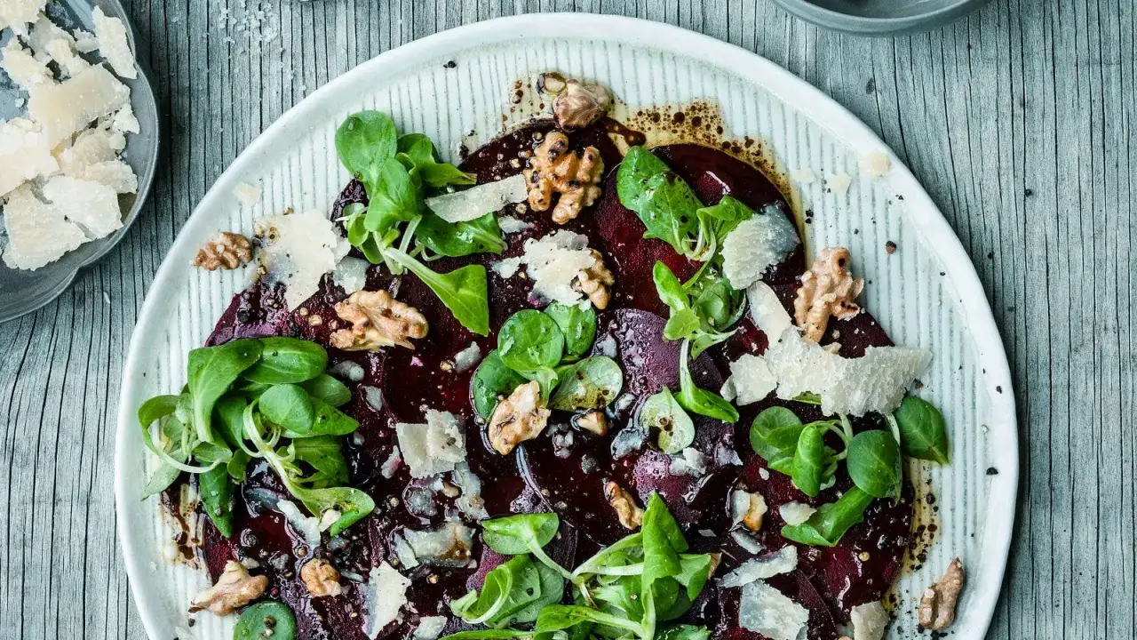 Rote Bete Carpaccio vegan mit Walnüssen, Rucola und gehobeltem Parmesan auf einem Teller.