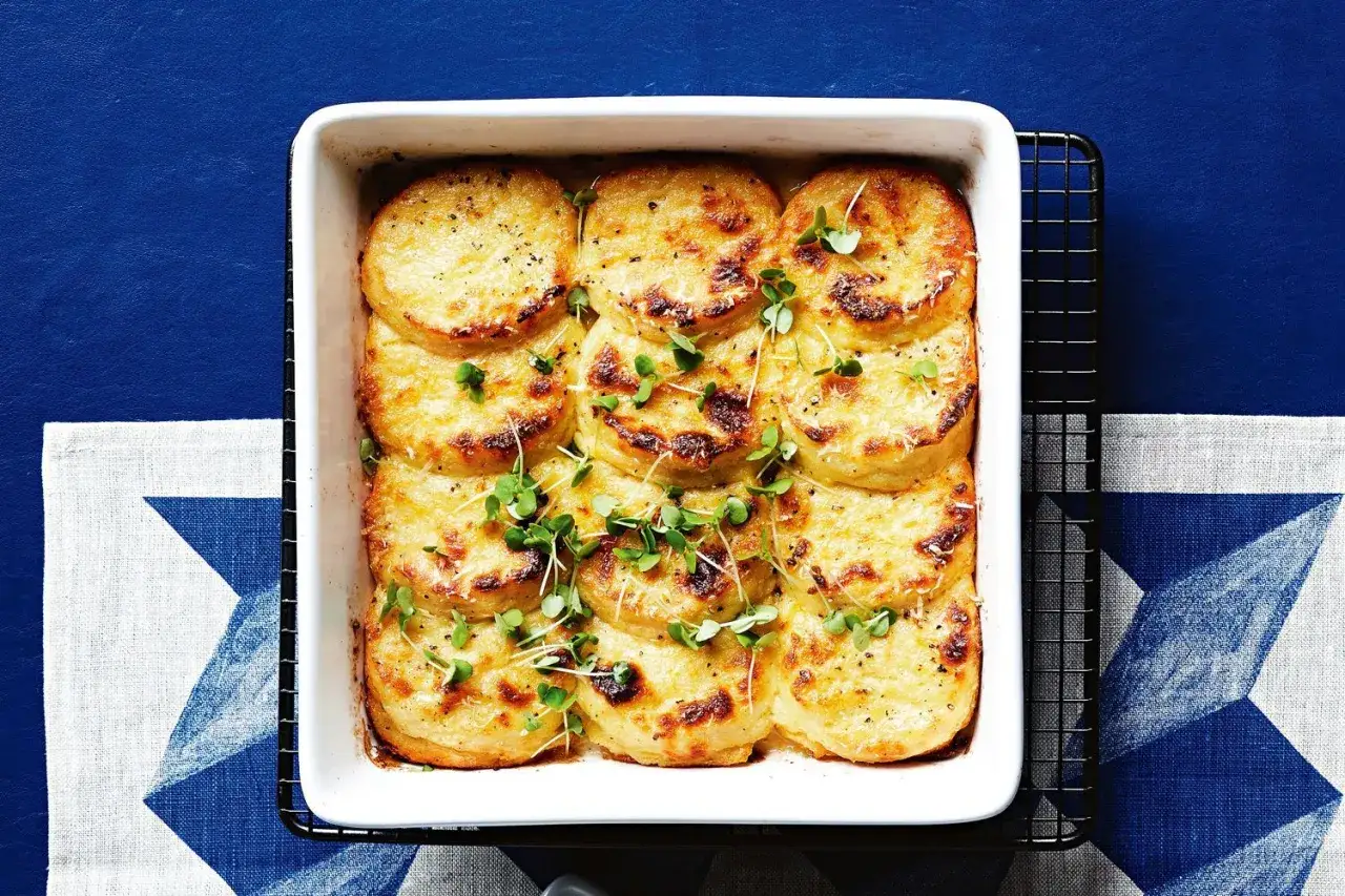Gyllene, gratinerade skivor av gnocchi alla romana i en vit ugnsform, toppade med färska groddar.