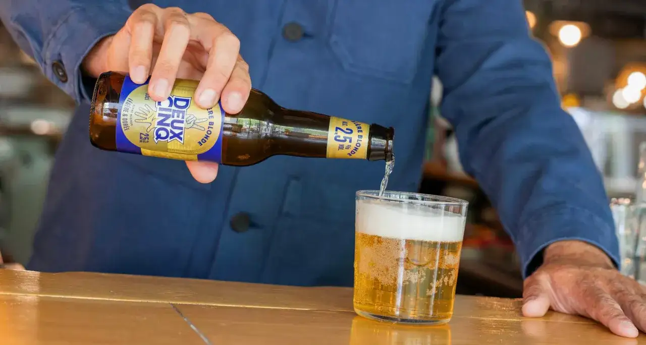 Une main verse une bière blonde légère et dorée, une bière peu alcoolisée à 2.5% vol, dans un verre.