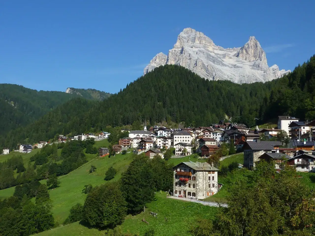 Un pittoresco villaggio alpino, con il rifugio Venezia in primo piano, incastonato tra verdi pendii e dominato da imponenti vette rocciose.