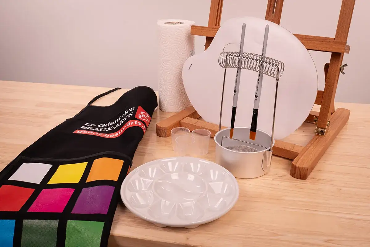 Un tablier coloré, une palette, des pinceaux, des gobelets et un rouleau d'essuie-tout sont prêts pour le materiel peinture huile.