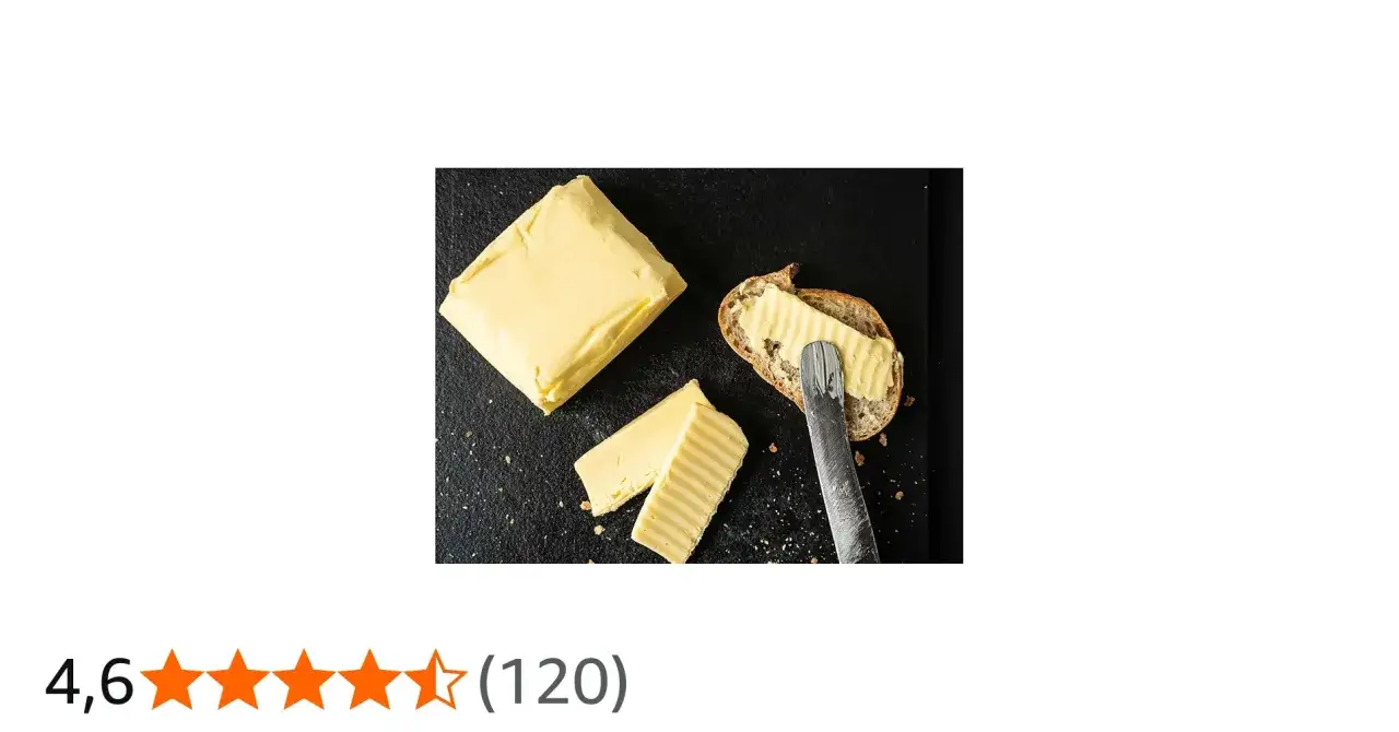 Ein Block und zwei Scheiben butter aus rohmilch auf dunklem Untergrund. Eine Scheibe Brot wird gerade mit Butter bestrichen.