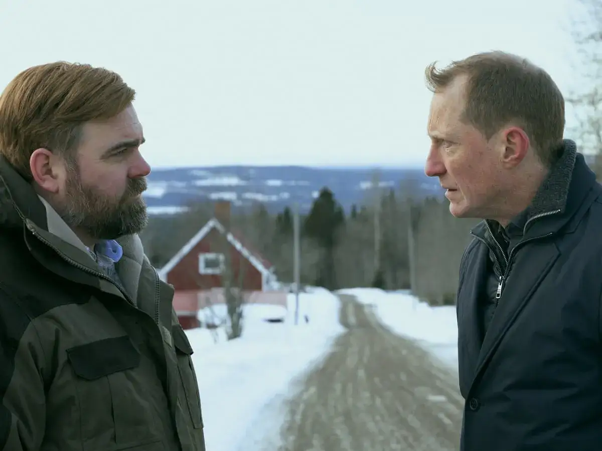 Två män står vända mot varandra i ett snöigt landskap. En väg leder upp mot ett rött hus. **The shadow line** mellan dem antyder en spänd situation.