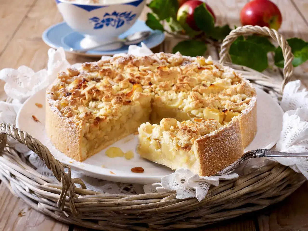 Omas weltbester Apfelkuchen mit Streuseln und Mandeln, ein St&uuml;ck herausgeschnitten, daneben eine Sch&uuml;ssel mit Vanillesauce.