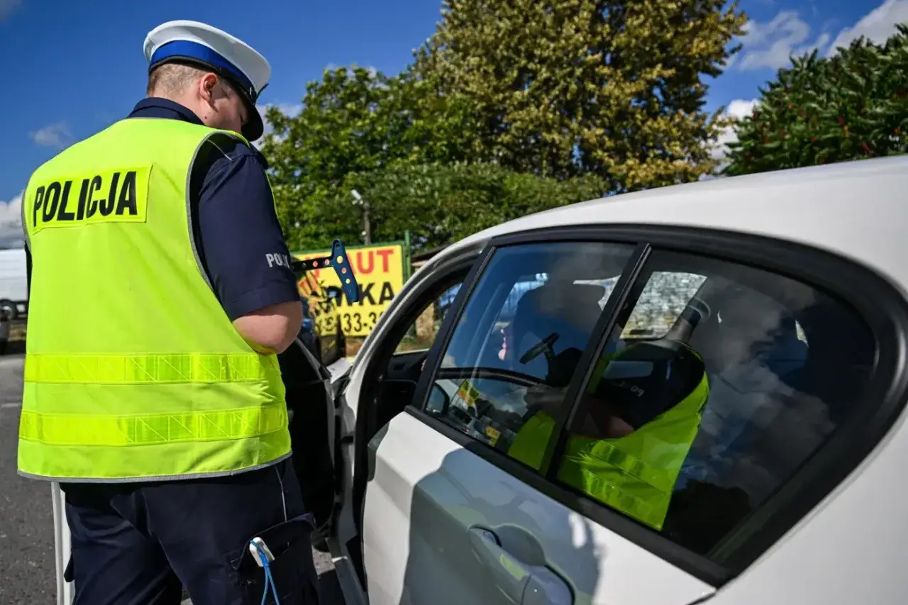 Policjant kontroluje dokumenty kierowcy. Może to być kontrola dotycząca braku przeglądu, za co grozi kara.