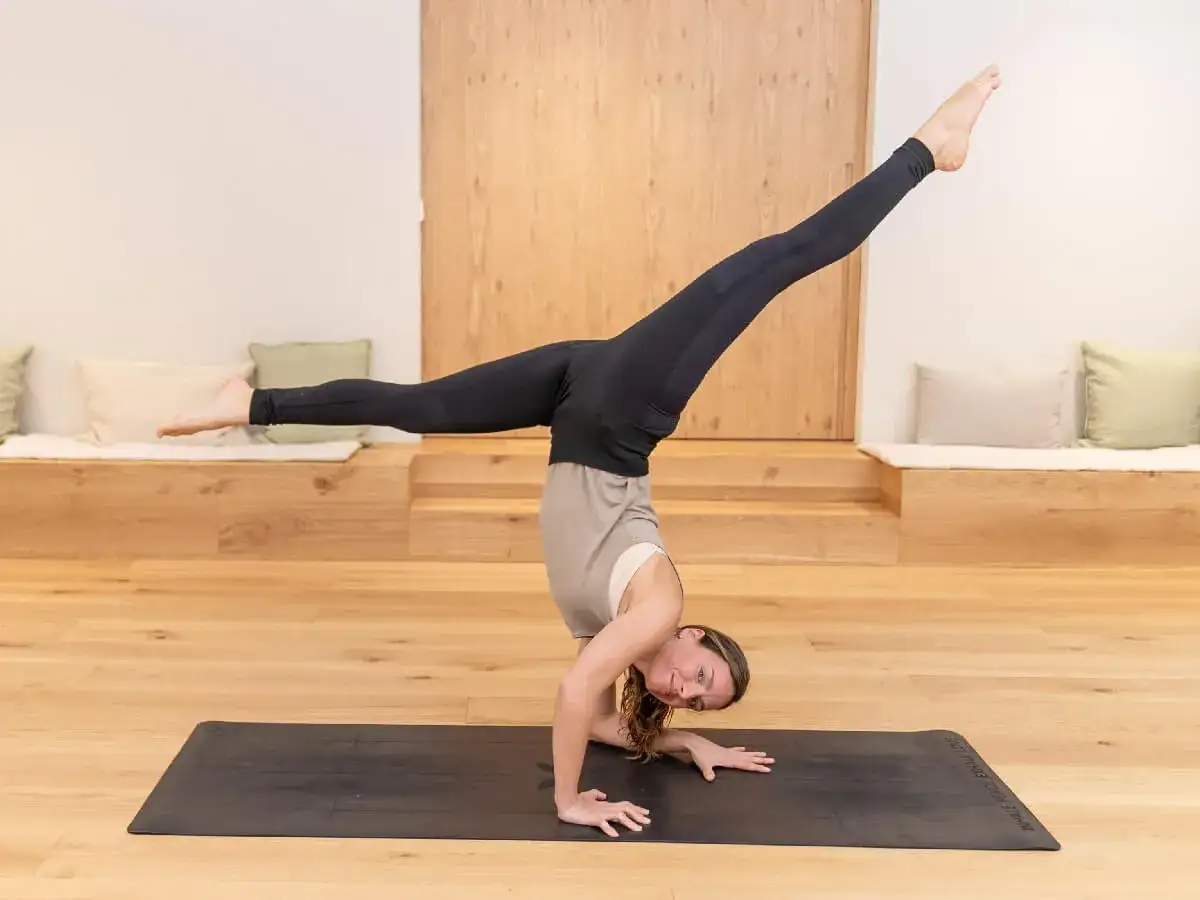 Mujer en equilibrio sobre sus manos, con una pierna extendida hacia arriba. Una demostración de fuerza y flexibilidad, como en el **power yoga que es** una disciplina intensa.