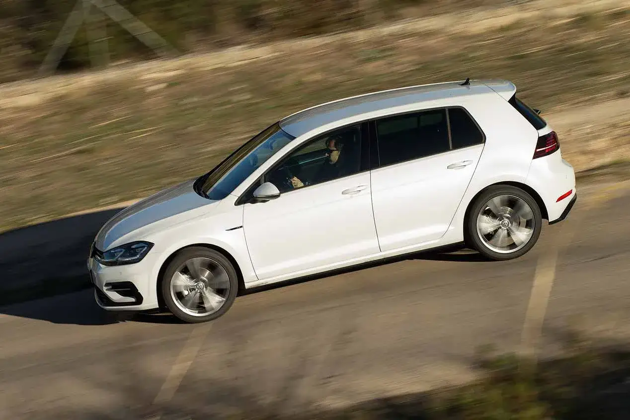 Un Golf 1.5 TSI blanco en movimiento por una carretera rural, con el sol brillando sobre su carrocería.