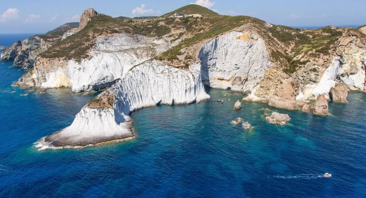 Scogliere bianche a picco sul mare blu intenso di Ponza. Un piccolo gozzo solca le acque cristalline.