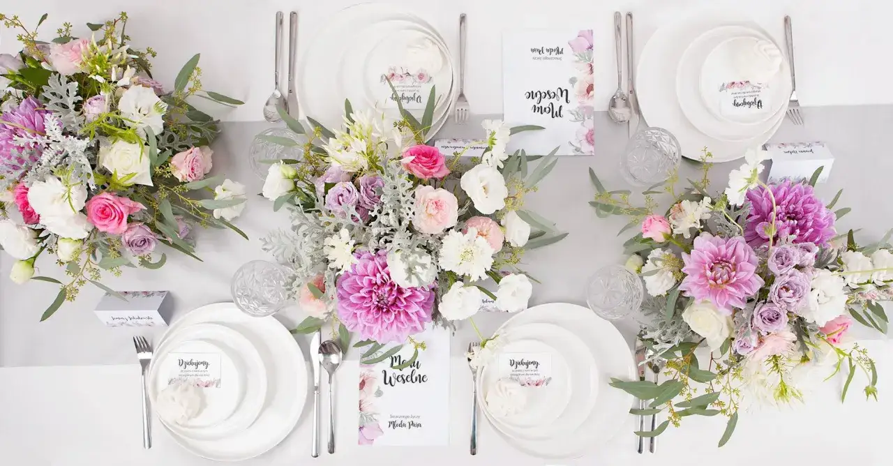 Stół weselny w kwietniu ozdobiony bukietami różowych i fioletowych kwiatów. Eleganckie nakrycia, menu i winietki zapowiadają uroczystość.