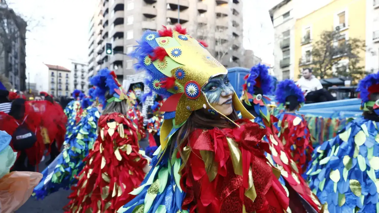 Desfile de coloridos disfraces en los carnavales de Zaragoza. Una persona con un elaborado tocado de pájaro sonríe a la cámara.