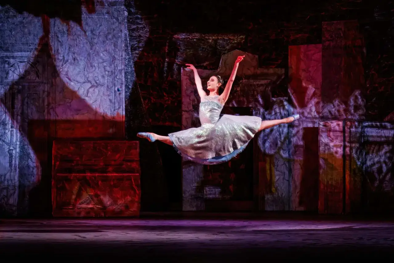 En ballerina i en glittrig klänning gör ett elegant hopp på scenen. En magisk föreställning av kungliga baletten.