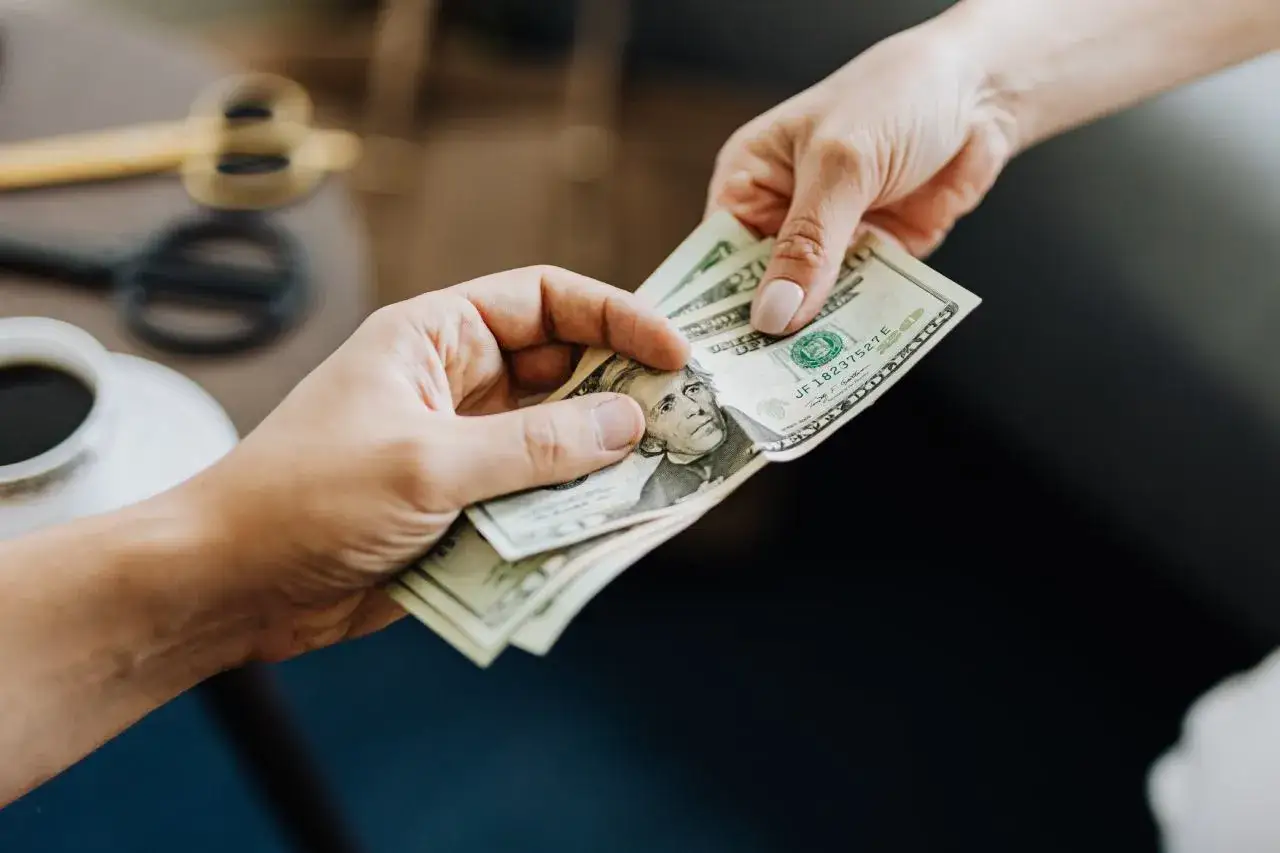 Dwie ręce przekazują sobie banknoty. To symbol sprawdzone pożyczki społecznościowe, gdzie ludzie pomagają sobie nawzajem finansowo.