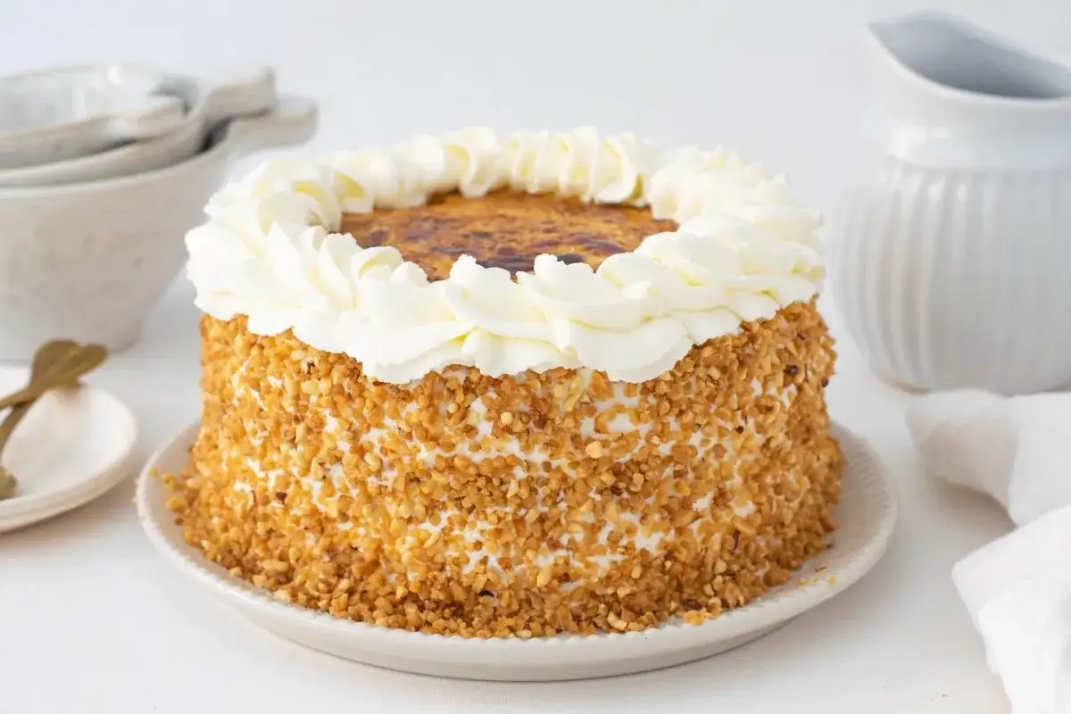 Tarta San Marcos con cobertura crujiente de frutos secos y un borde de nata montada. La parte superior tiene un glaseado dorado y caramelizado.