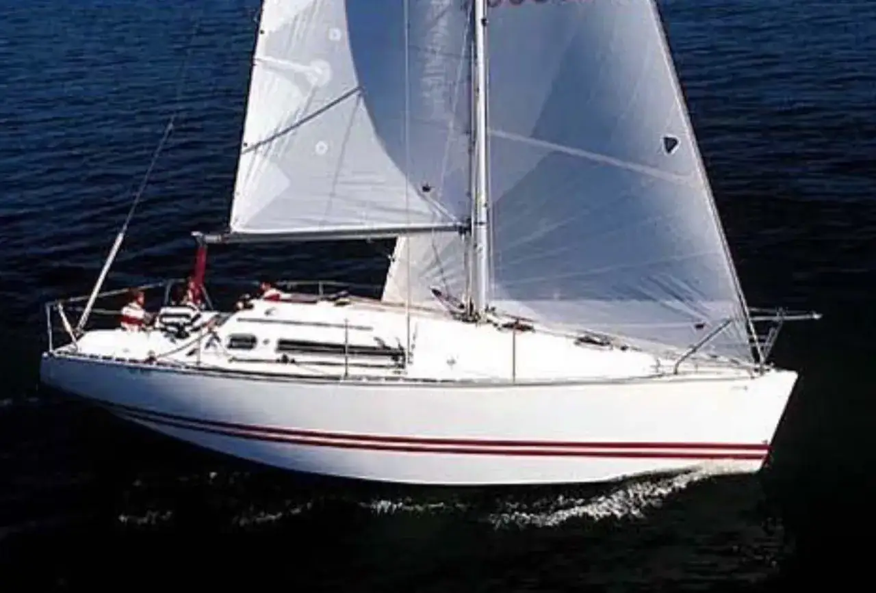 Voilier blanc avec deux personnes à bord, naviguant sur une mer sombre. Les avis sur le Sun Fast 32 confirment sa rapidité.