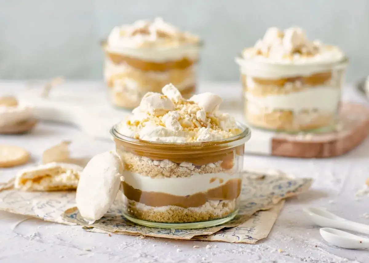Postres en vaso con capas de bizcocho, crema y dulce de leche, coronados con merengue y un toque de polvito canario.