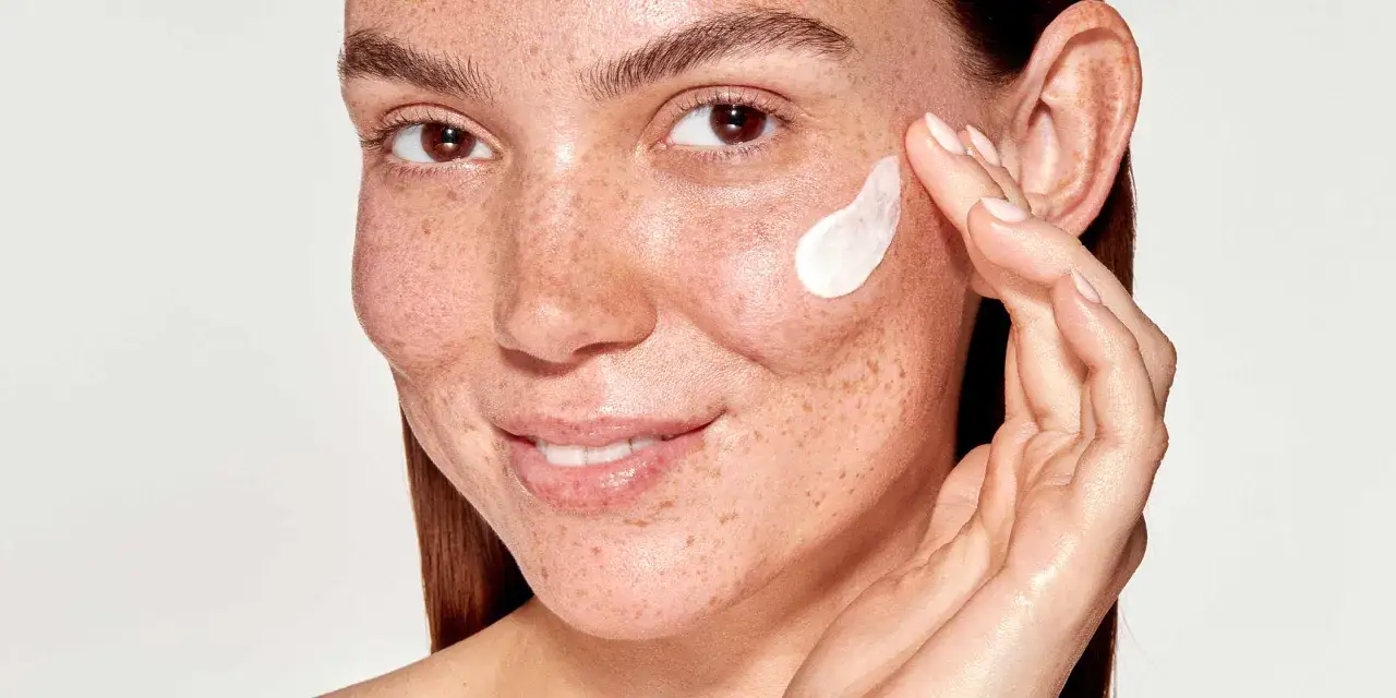 Une femme au visage parsem&eacute; de taches brunes applique une cr&egrave;me hydratante.