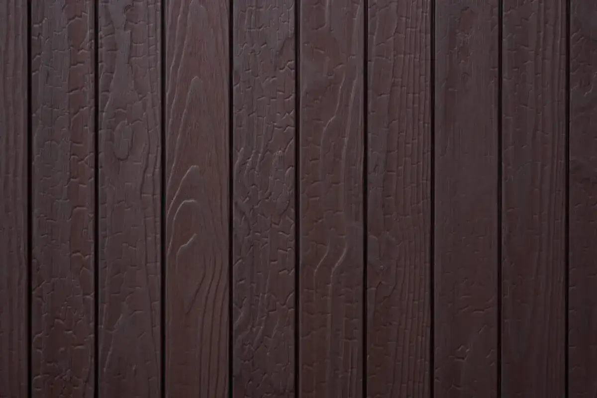 Tavolato scuro con venature evidenti, che ricorda il **legno bruciato** per il suo aspetto vissuto e le crepe superficiali.