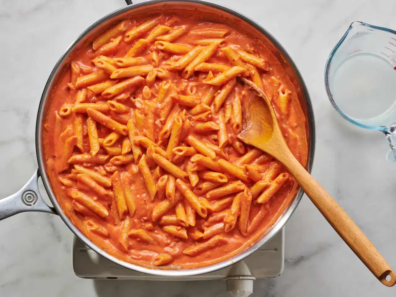 En stor panna med krämig vegetarisk pasta i en ljusrosa tomatsås. En träsked ligger i pannan.