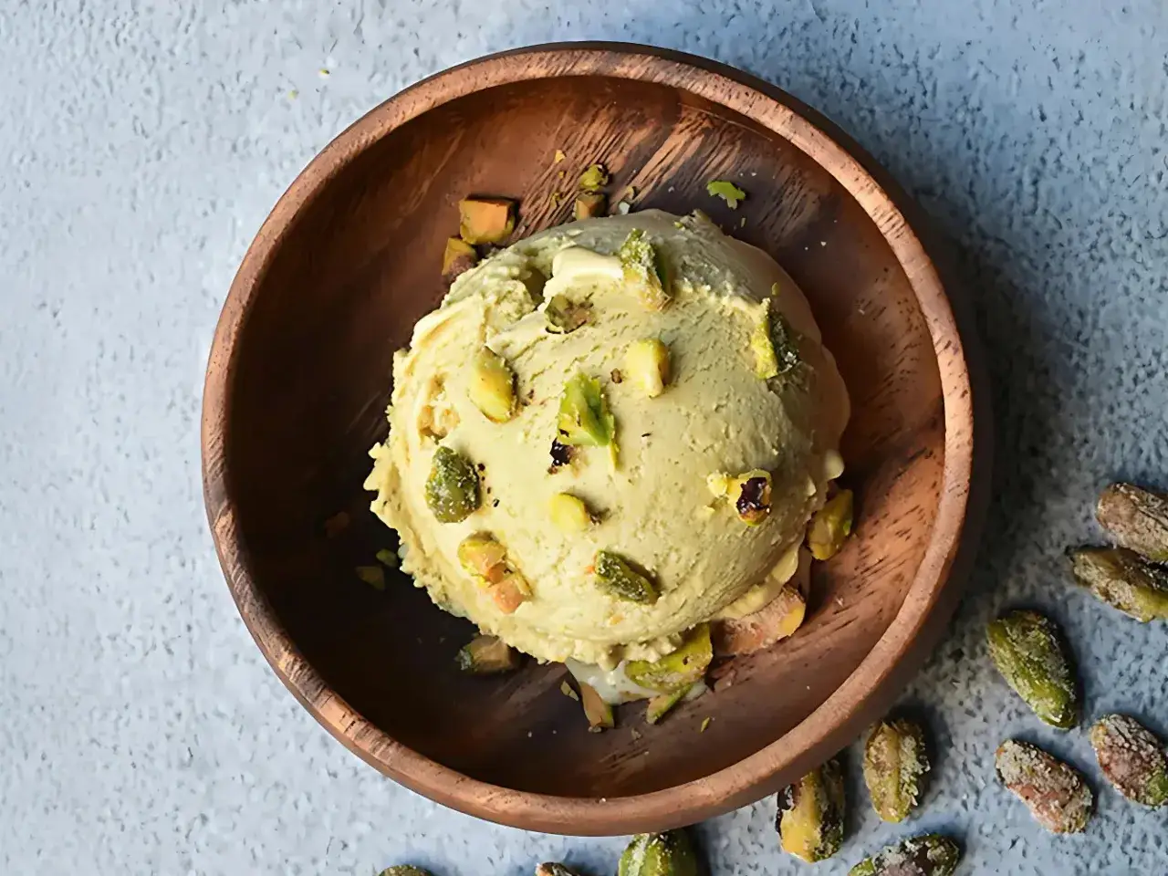 Cremoso helado de pistacho, con trozos de pistacho esparcidos, servido en un cuenco de madera.