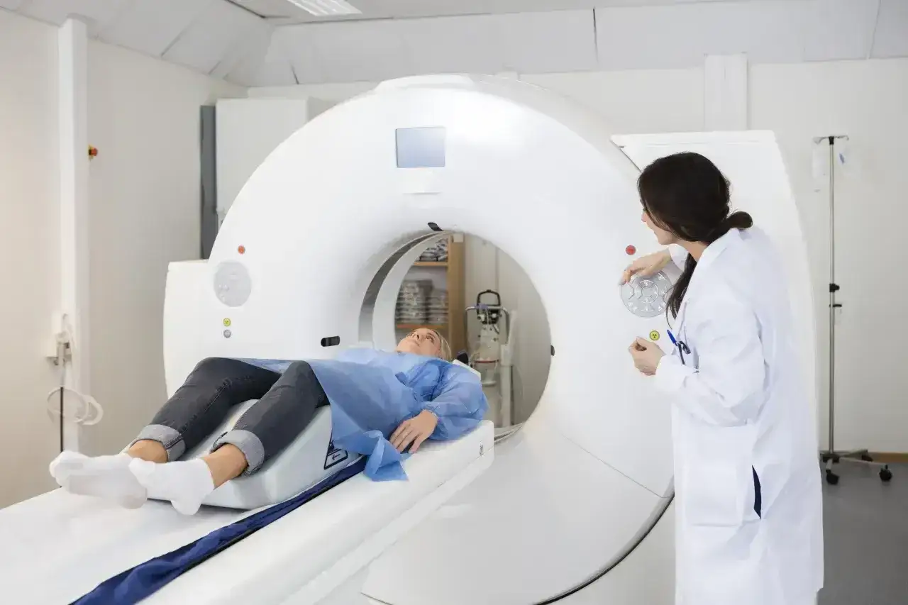 Pacjentka na stole do rezonansu magnetycznego, lekarz przygotowuje badanie. Po podaniu kontrastu mogą wystąpić dolegliwości.