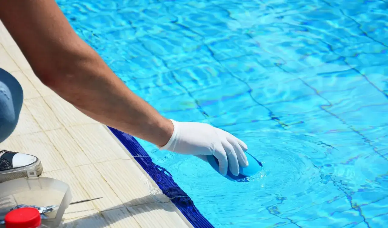 Mano con guanto bianco immerge un tester nell'acqua della piscina per controllarne il ph.
