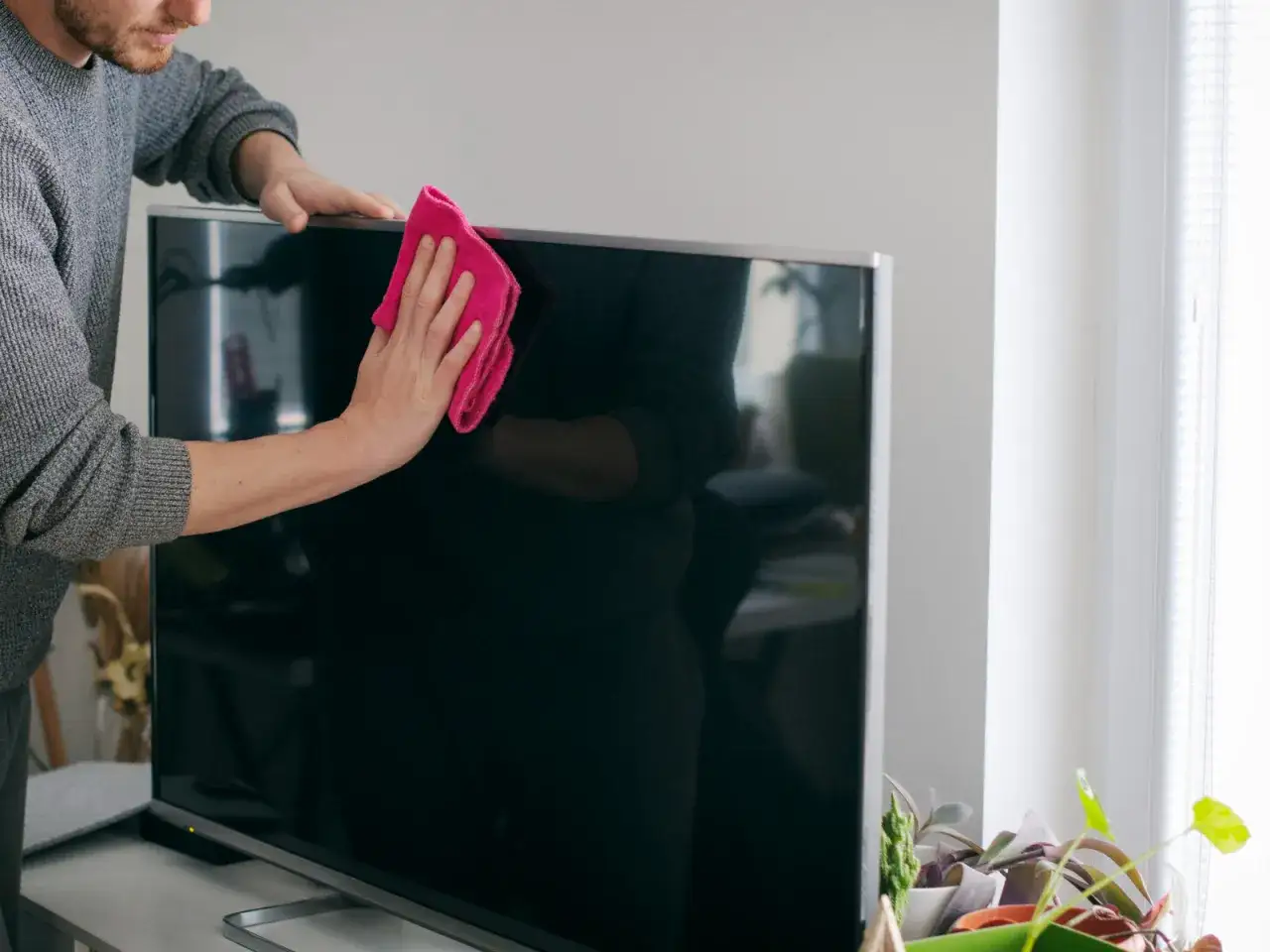 Mężczyzna czyści ekran telewizora różową ściereczką z mikrofibry. Dowiedz się, czym umyć ekran telewizora, by był idealnie czysty.