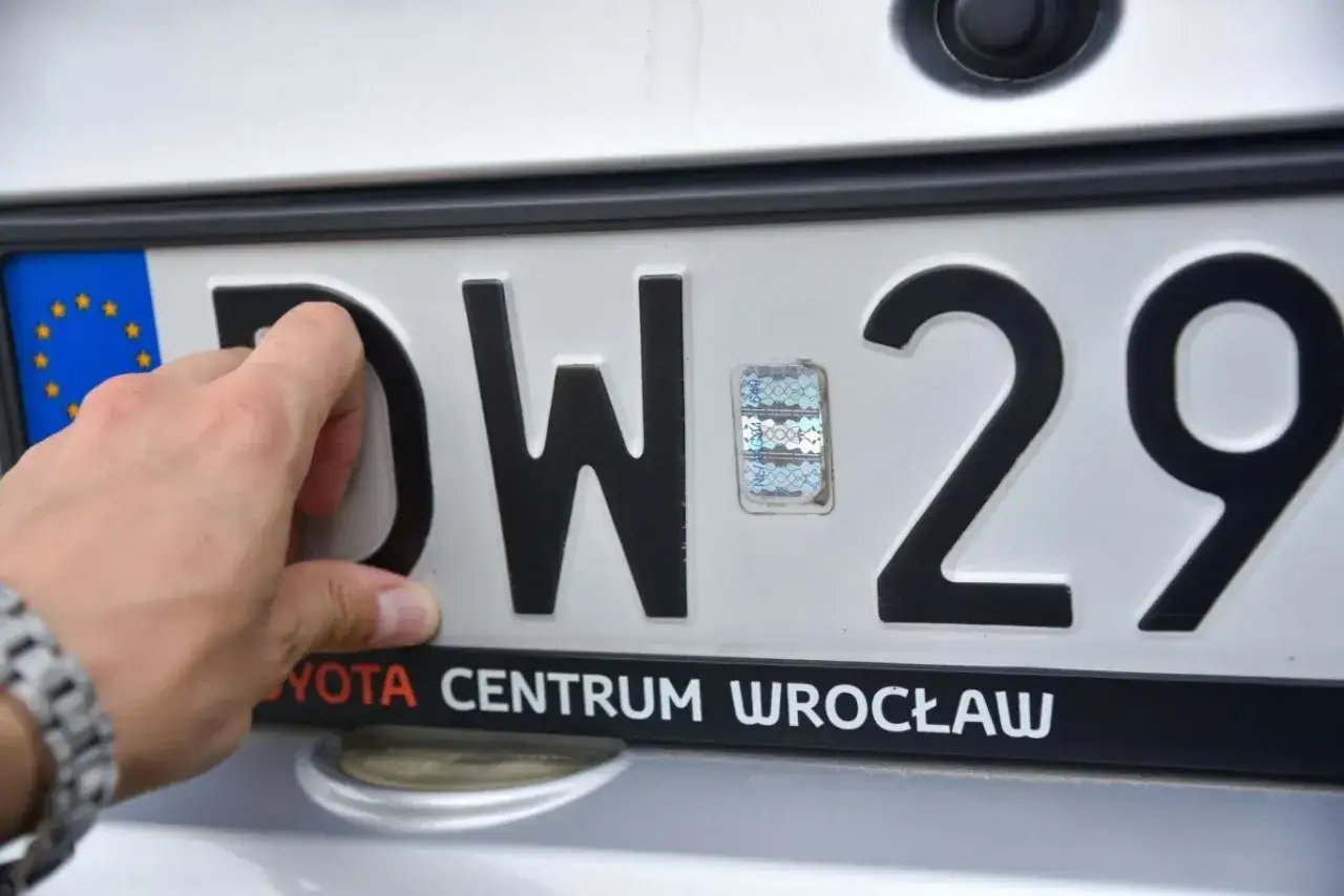 Dłoń poprawia hologram na tablicy rejestracyjnej DW 29. Pgo rejestracja w Toyota Centrum Wrocław.